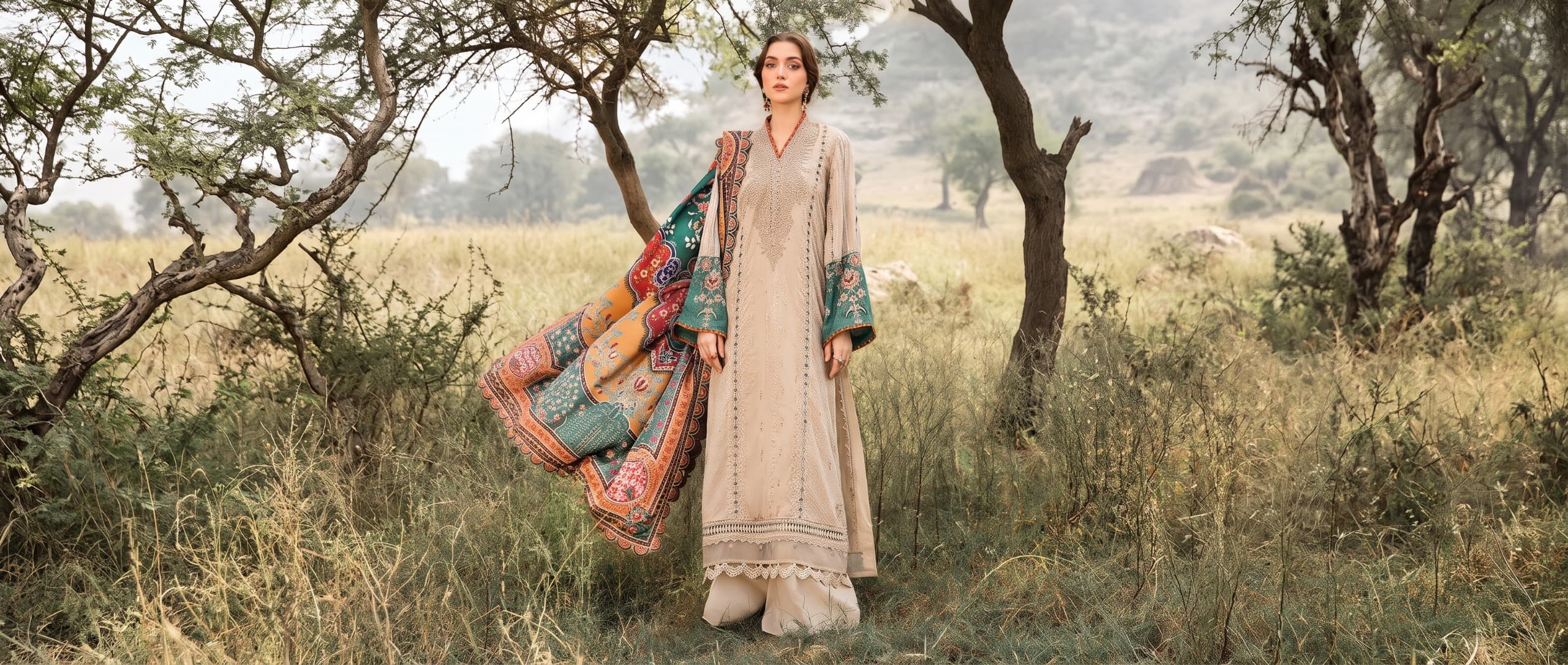 Model in embroidered beige suit with printed shawl in a field